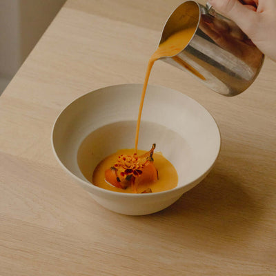 Set of 4 Neo Bowls in White Matte with soup being poured into one on a wooden table.