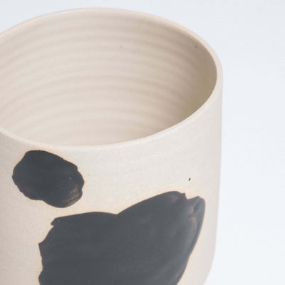 Close-up of a beige stoneware cup with black brush strokes and textured interior design, perfect for modern decor.
