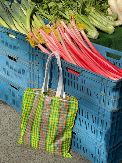 Bunte Einkaufstasche neben frischem Rhabarber und Gemüse auf einem Markt, für nachhaltigen Einkauf.