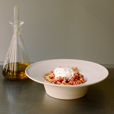 Handgemachte Keramik Pasta Schale in Creme mit nuddelförmigem Pasta und Sahne-Topping.