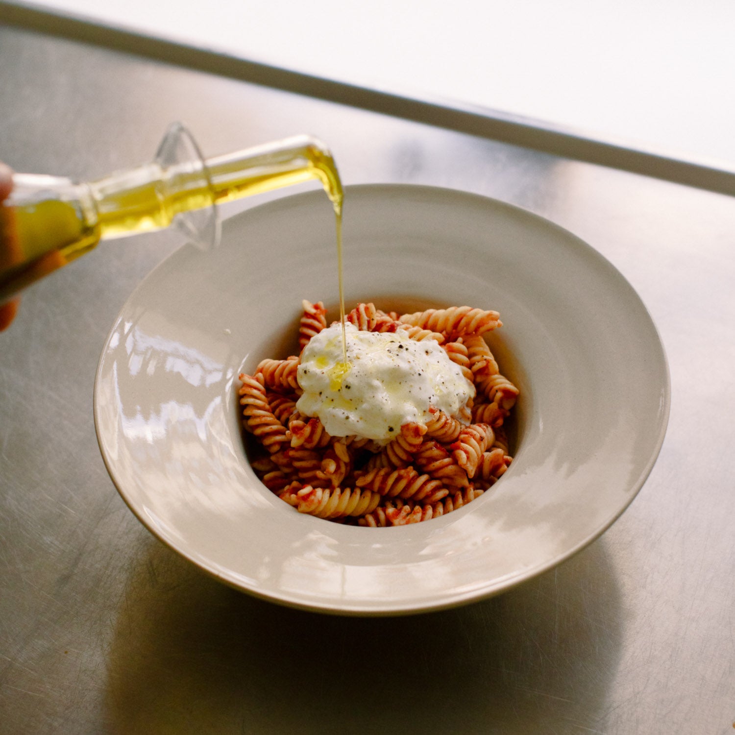 Handgemachte Keramik Pasta Schale mit farbenfrohen Fusilli und frischem Käse, Olivenöl wird hinzugefügt.