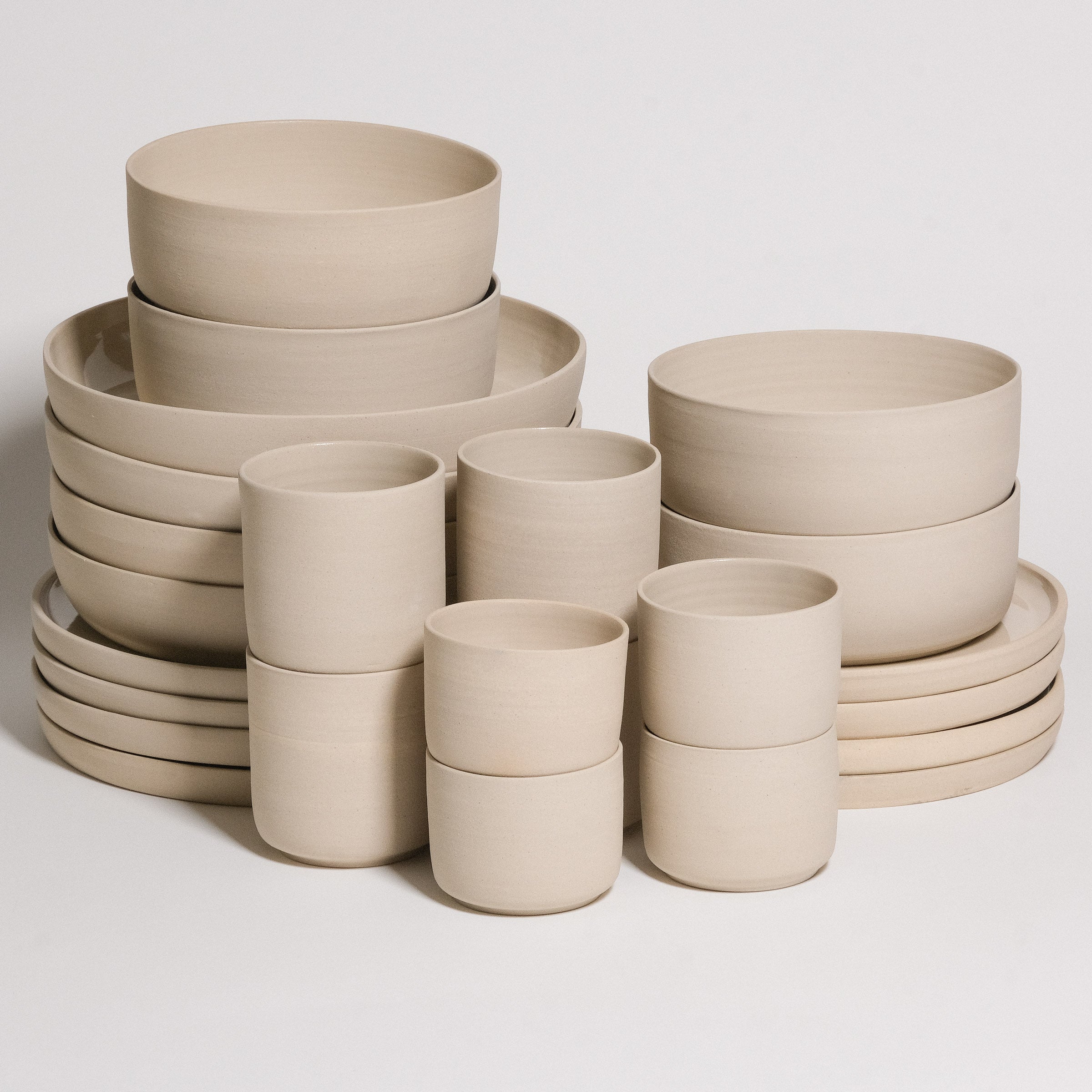 Geschirrset Creme 24-teilig aus grauem Steinzeugton, bestehend aus Schalen und Tellern.
